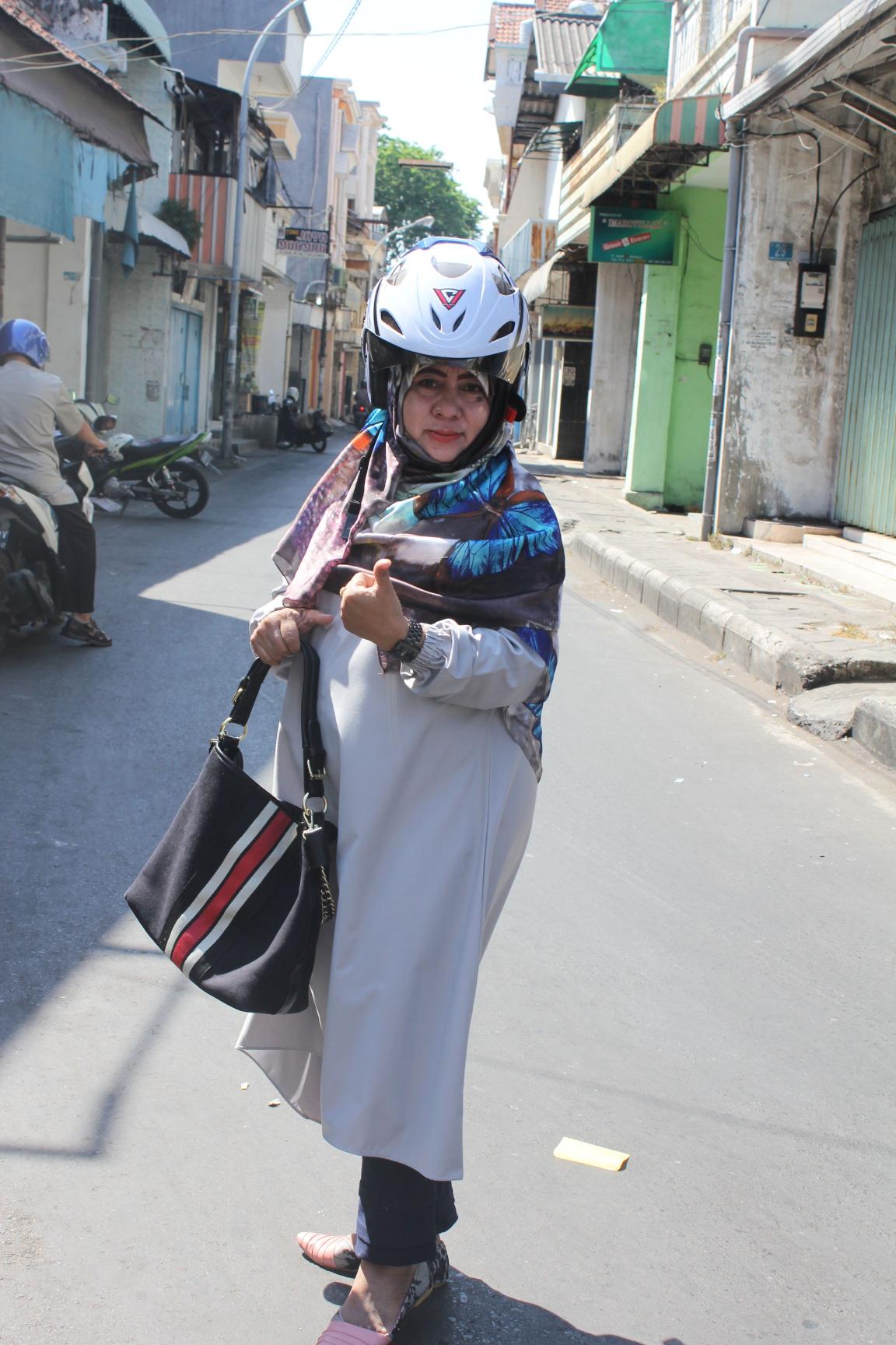 Frau aus Indonesien zeigt Daumen hoch und hat einen Helm auf