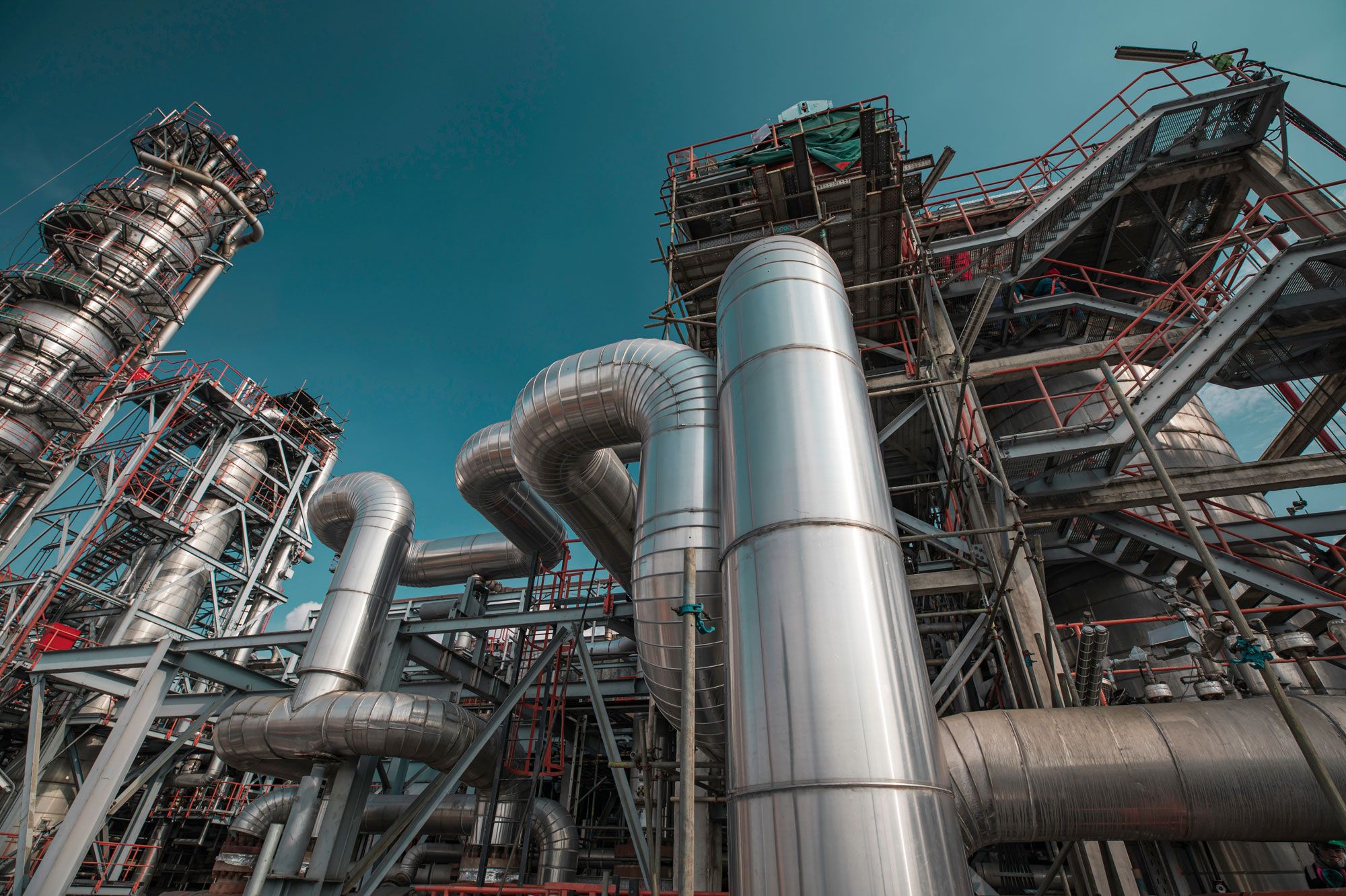 Eine Nahaufnahme einer modernen Industrieanlage mit markanten Metallrohren und hoch aufragenden Strukturen unter blauem Himmel.